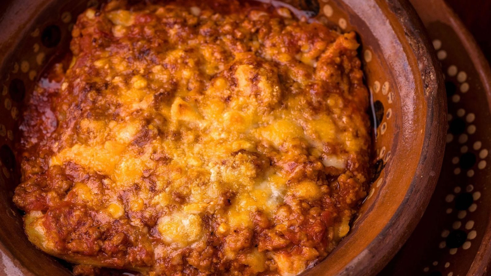 Lasaña a la boloñesa recién horneada y gratinada en cazuela de barro