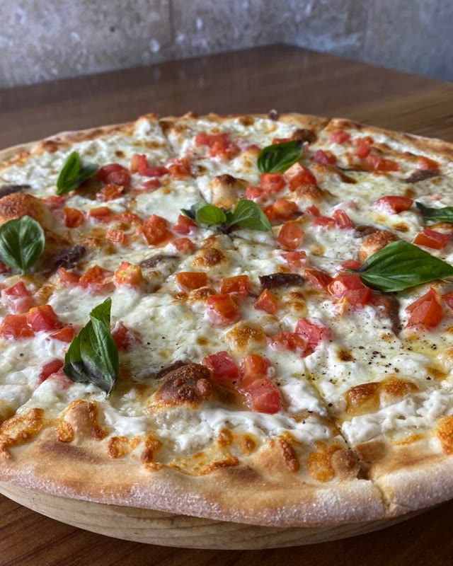 Pizza con jitomate fresco y albahaca, recién servida en la mesa